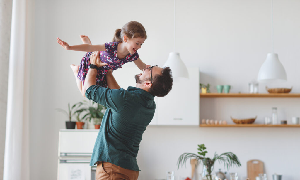 A father lifting his laughing young daughter in a bright kitchen